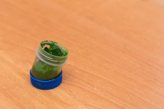 An old open jar of green gouache for painting. Side view of a half-empty can of gouache paint. There is empty copy space.