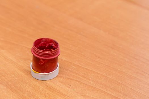 An old open jar of red gouache for painting. Side view of a half-empty can of gouache paint. There is empty copy space.