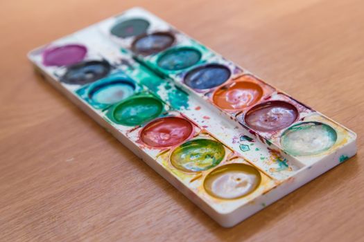 A set of old watercolor paints for painting. Top view of half-empty jars of watercolors. Flat layout on the table.