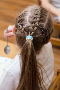 Close-up of a hairstyle with pigtails on the girl's head and a ponytail of hair. Hair styling is done with hairpins and an elastic band. Only the back of the head with a haircut.