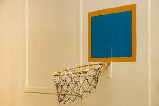 An old basketball hoop against a yellow wall. The basketball basket sagged down. The back is a blue square with orange outline.