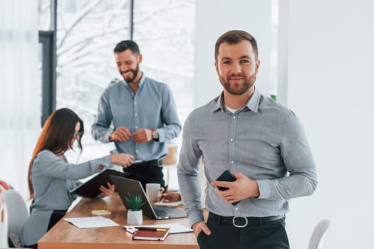 Man standing and smiling. Group of business people that working on the project in the office.
