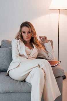 Sitting on the sofa. Business woman in formal clothes is indoors posing for the camera.