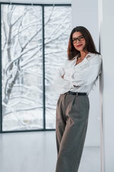 Standing near window. Business woman in formal clothes is indoors posing for the camera.