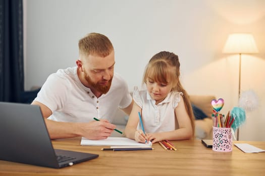 Using laptop. Father with his little daughter is at home together.