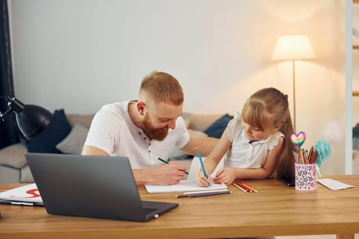 Using laptop. Father with his little daughter is at home together.