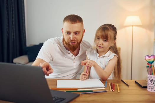Using laptop. Father with his little daughter is at home together.