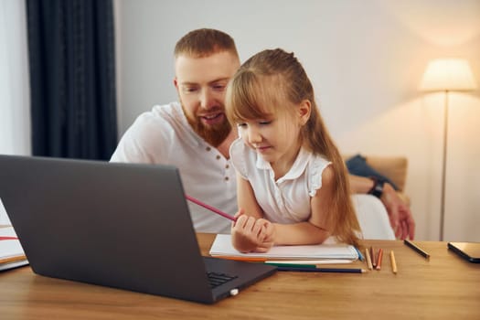 Using laptop. Father with his little daughter is at home together.
