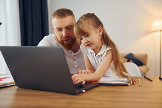 Using laptop. Father with his little daughter is at home together.