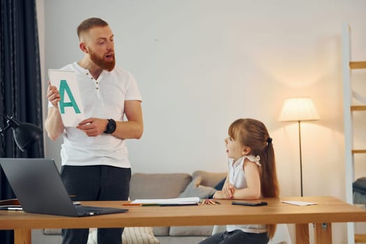 Little girl sitting by the table. Father with his little daughter is at home together.