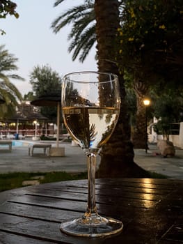 Glass of white wine on the wooden table, reflection of palm trees in a glass of white wine. High quality photo