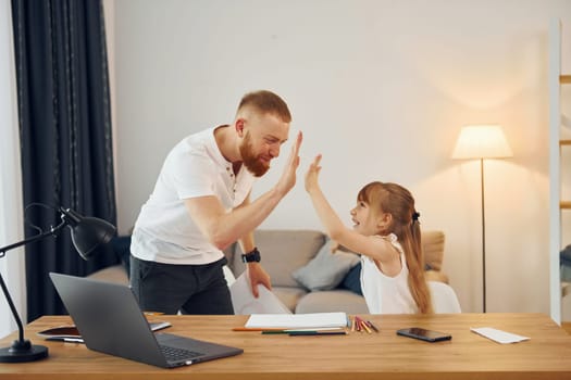 Little girl sitting by the table. Father with his little daughter is at home together.