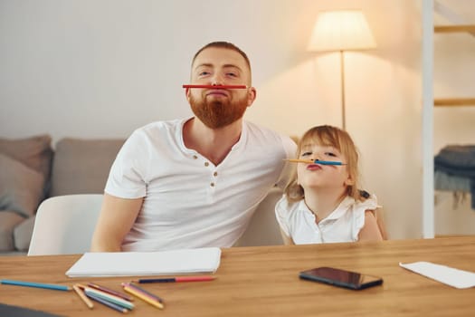 Little girl sitting by the table. Father with his little daughter is at home together.