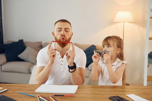Little girl sitting by the table. Father with his little daughter is at home together.