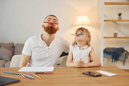 Sitting by the table and having fun. Father with his little daughter is at home together.