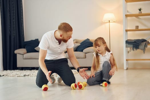 With throwing balls. Father with his little daughter is at home together.