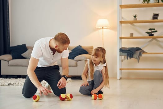 With throwing balls. Father with his little daughter is at home together.