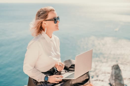 Business woman on nature in white shirt and black skirt. She works with an iPad in the open air with a beautiful view of the sea. The concept of remote work