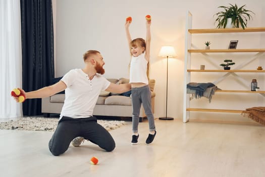 With throwing balls. Father with his little daughter is at home together.