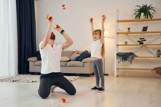 With throwing balls. Father with his little daughter is at home together.