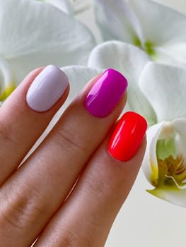 Beautiful Female close up summer colored pink red light pink nails manicure, orchid flower on the light background