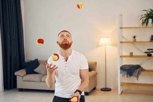 A man in casual clothes throws balls at home.