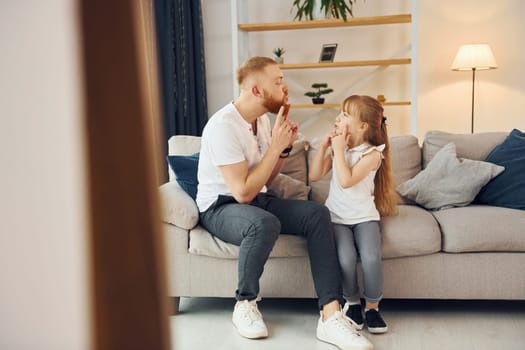 On the sofa. Having fun. Father with his little daughter is at home together.