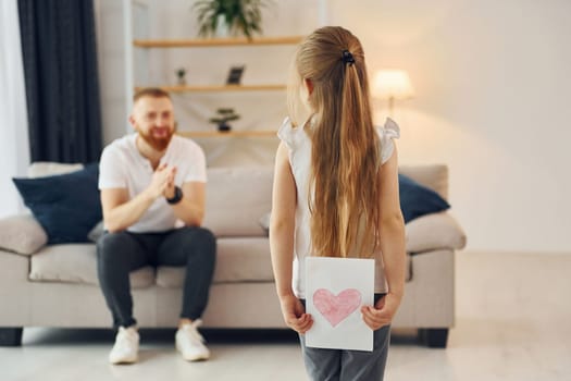 Little girl have gift for man. Father with his little daughter is at home together.