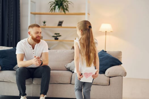 Little girl have gift for man. Father with his little daughter is at home together.