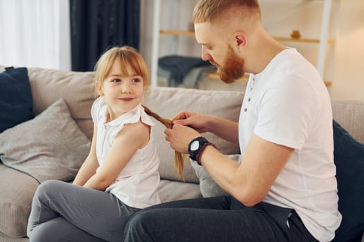 On the sofa. Having fun. Father with his little daughter is at home together.