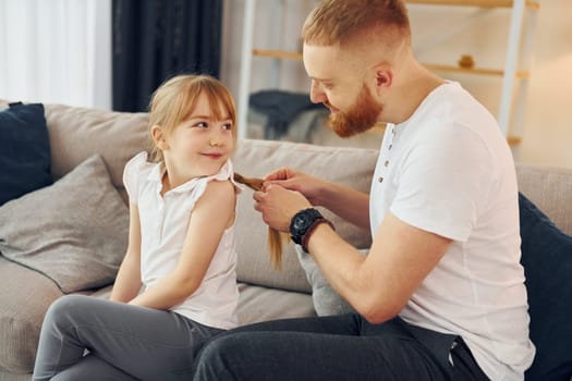Man braids the braids. Father with his little daughter is at home together.