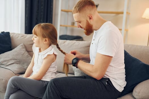 Man braids the braids. Father with his little daughter is at home together.