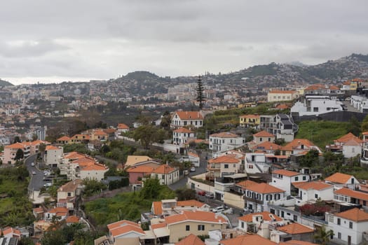 A rural village perched atop a hill, with picturesque architecture and lush trees surrounded by winding roads. Madeira, Portugal