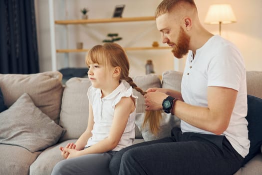 Man braids the braids. Father with his little daughter is at home together.