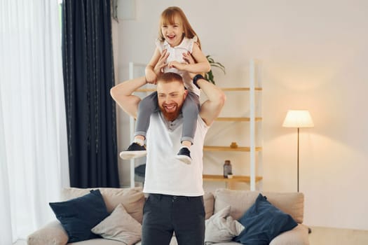 Girl sitting on the shoulders. Father with his little daughter is at home together.