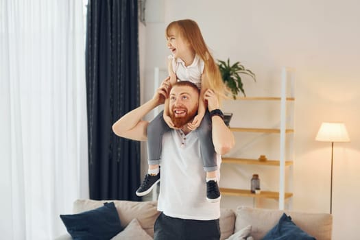 Girl sitting on the shoulders. Father with his little daughter is at home together.