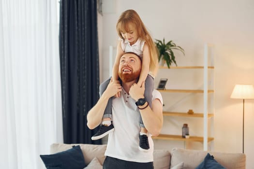Girl sitting on the shoulders. Father with his little daughter is at home together.