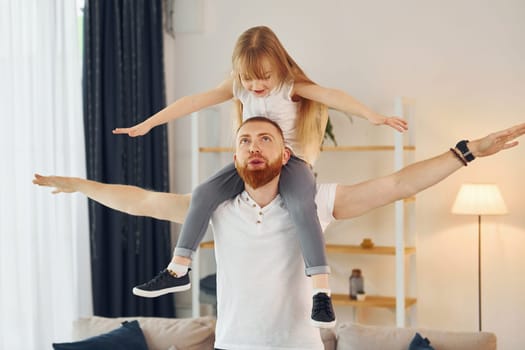Girl sitting on the shoulders. Father with his little daughter is at home together.