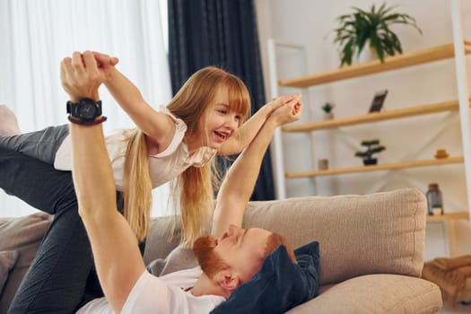 Laying down on the sofa. Father with his little daughter is at home together.