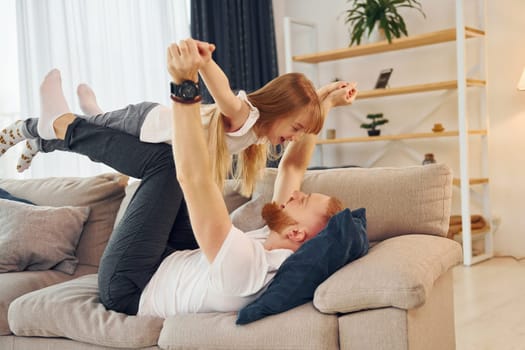 Laying down on the sofa. Father with his little daughter is at home together.