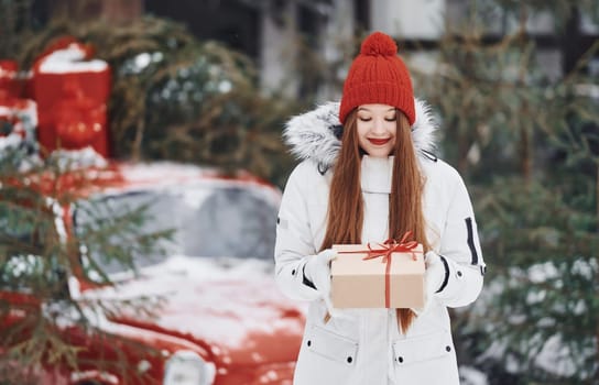 Holding present box. Happy young woman standing outdoors and celebrating christmas holidays.