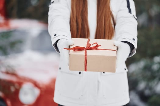 Holding present box. Happy young woman standing outdoors and celebrating christmas holidays.
