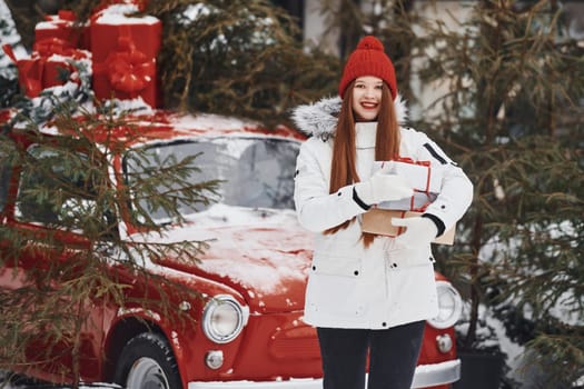 Holding present box. Happy young woman standing outdoors and celebrating christmas holidays.
