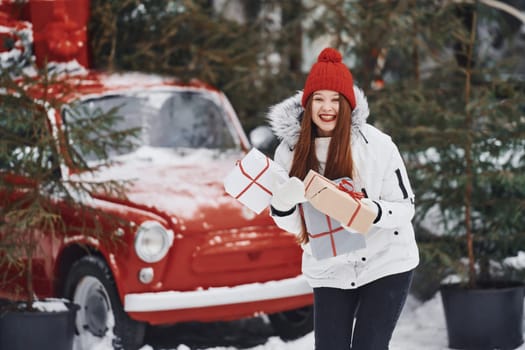 Holding present box. Happy young woman standing outdoors and celebrating christmas holidays.