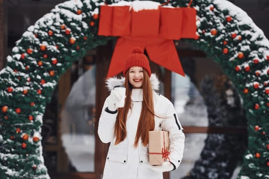 Holding present box. Happy young woman standing outdoors and celebrating christmas holidays.
