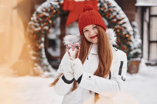 Holding sweets. Happy young woman standing outdoors and celebrating christmas holidays.