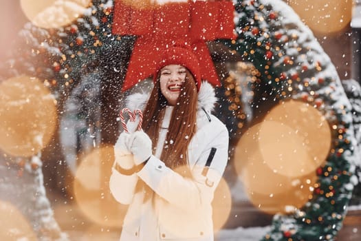 Holding sweets. Happy young woman standing outdoors and celebrating christmas holidays.