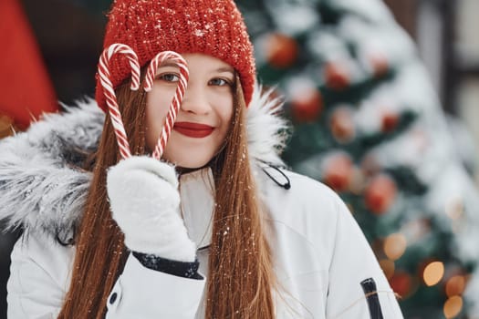 Holding sweets. Happy young woman standing outdoors and celebrating christmas holidays.