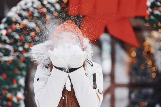Playing with snow. Happy young woman standing outdoors and celebrating christmas holidays.
