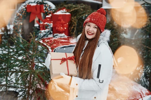 With gift box. Happy young woman standing outdoors and celebrating christmas holidays.